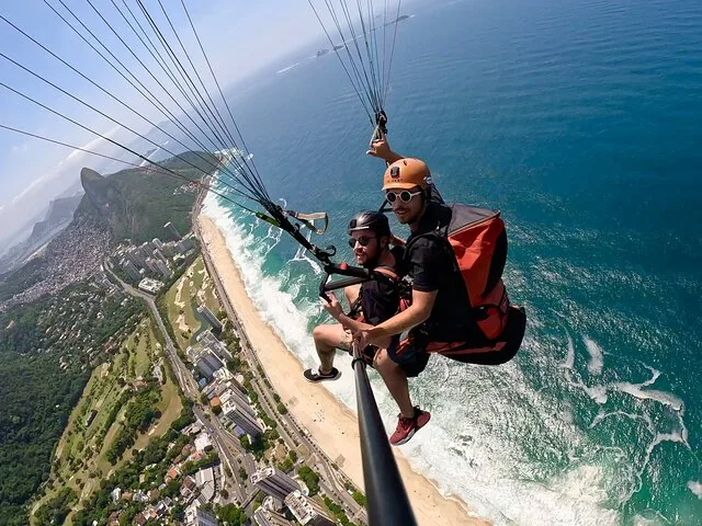 Selfie-Perspektive beim Tandem-Gleitschirmflug über einer belebten Küstenstadt und ihrem Strand