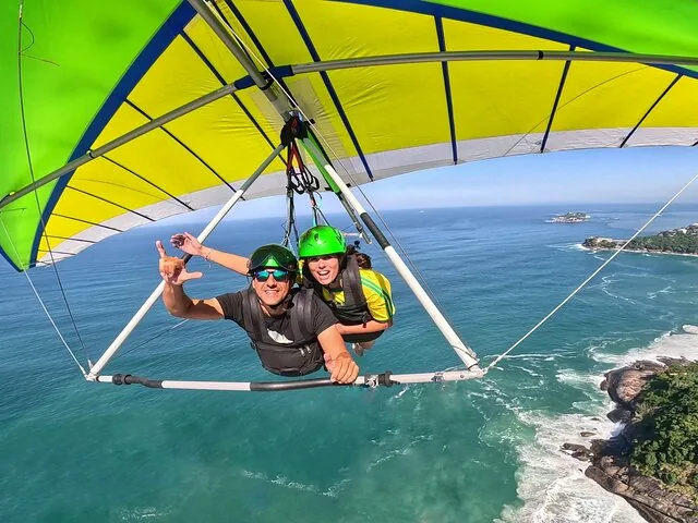 Passagier zeigt ein Shaka-Zeichen beim Tandem-Drachenflug über dem Meer