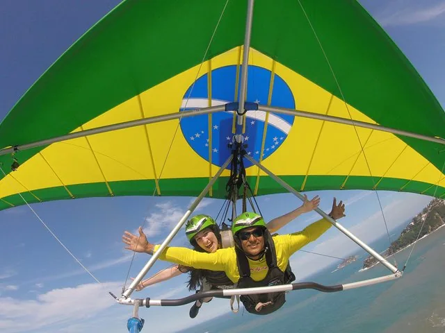 Tandem-Drachenflug über dem Ozean mit brasilianischer Flagge am Drachen