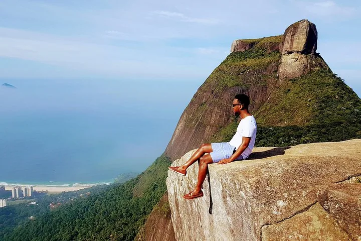 Mann sitzt am Klippenrand mit der Pedra Bonita im Hintergrund