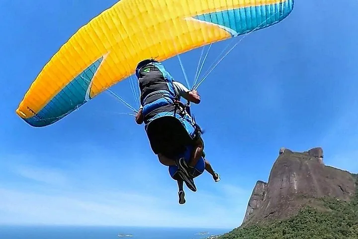 View from below of a tandem paraglider soaring near the Pedra Bonita mountain